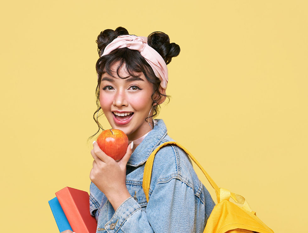Smiling woman in denim holds an apple and shopping bags against a yellow background, with books in hand.
