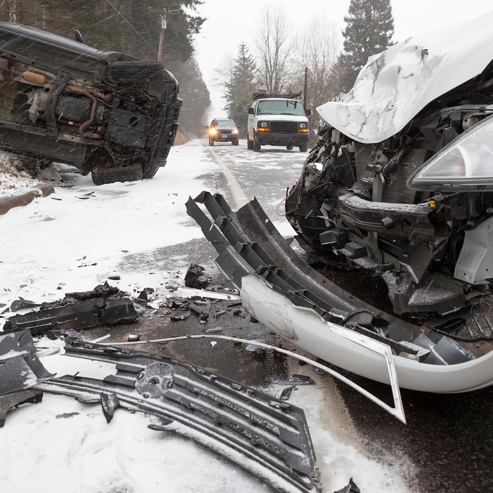 Car crash on a snowy road with one vehicle on its side and debris scattered. Other cars approach in the background, trees lining the road.