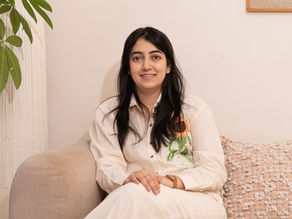 Designer Harshita Jhamtani seated in a cream interior beside a lit fluted ceramic floor lamp