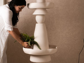 Harshita Jhamtani placing a fern into the planter bowl of a tall stacked stoneware totem floor lamp