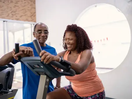  Mulher negra pedalando bicicleta ergométrica e o marido ao lado