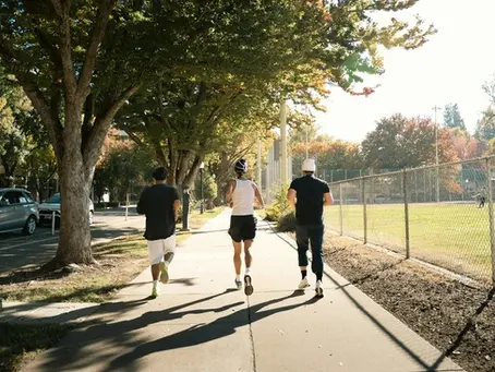 dois homens e uma mulher, vistos de costas correndo em um parque