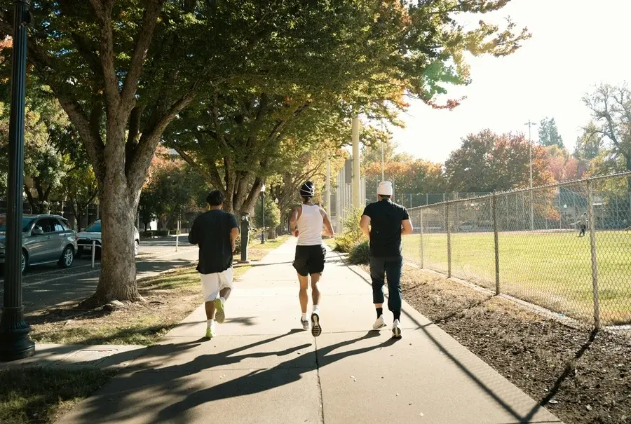 dois homens e uma mulher, vistos de costas correndo em um parque