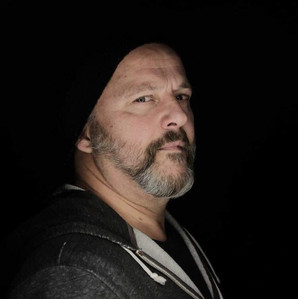 Portrait de Christian Beaulieu, membre de l’équipe des Cocagnes à Frelighsburg, photographié sur fond noir avec un éclairage doux mettant en valeur sa barbe poivre et sel et sa tuque noire. Souhaites-tu l’inclure dans un billet de blog sur un membre de l’équipe ou un portrait collaboratif? Je peux t’aider à le rédiger aussi!