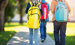 Three elementary school students wearing backpacks walking away
