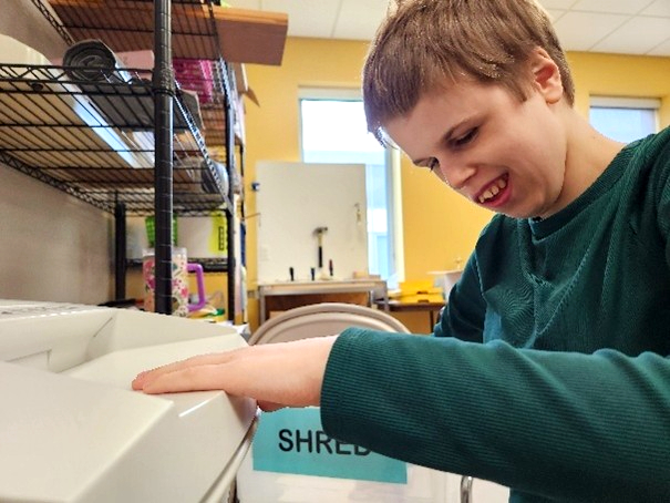 A girl smiles as she reaches out to touch a paper shredding machine_
