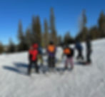 A young man on downhill skis holding onto a slider device for balance, standing with his guides after a fun run down the hill at Ski for Light in Black Hills, SD