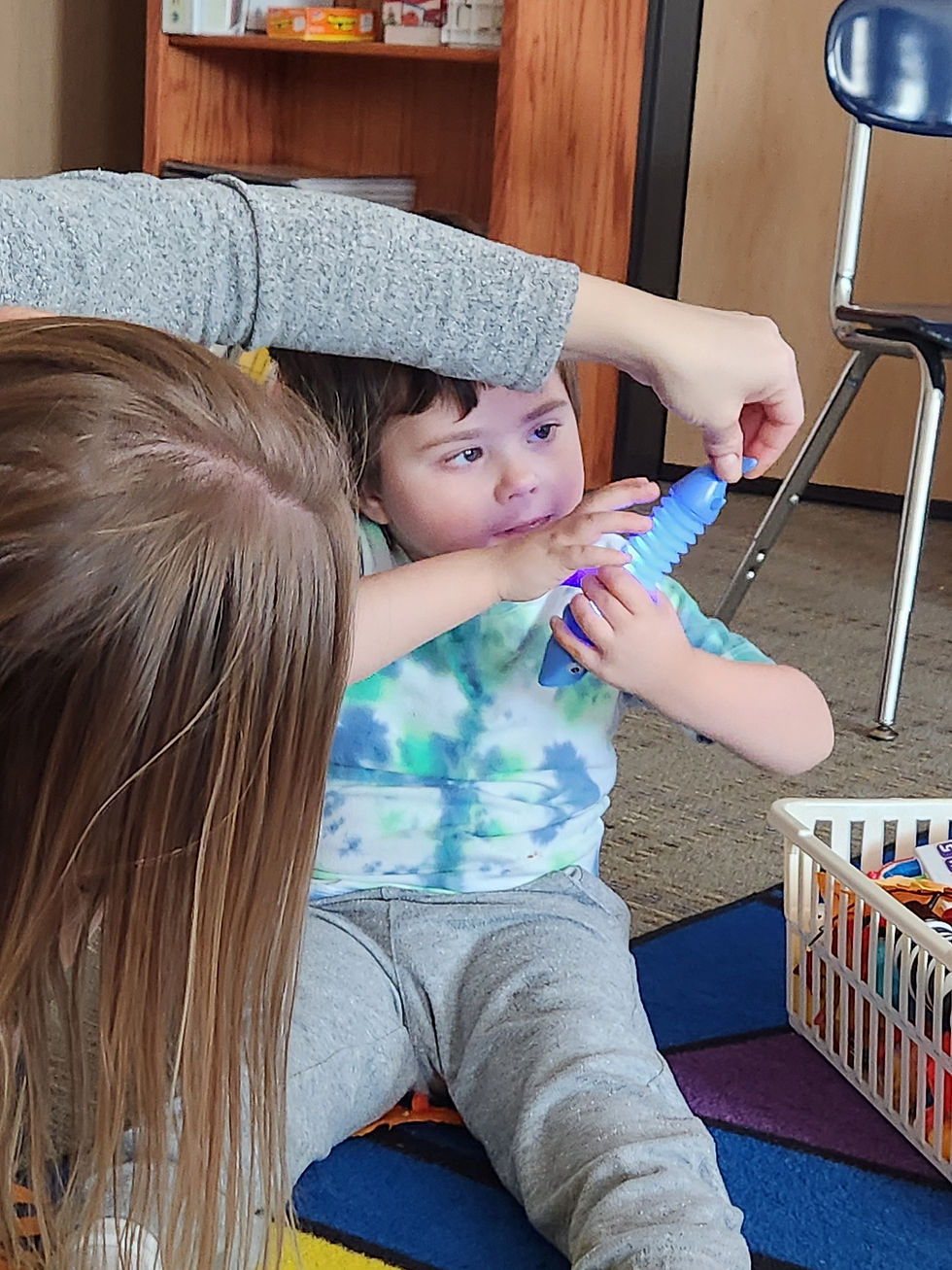 A young boy smiling while he explores a glowing pop tube toy held up by staff