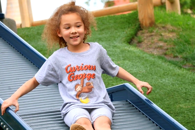 A young girl smiles as she slides down a large, open playground slide_