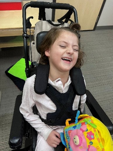 A young girl in a wheelchair laughs while playing with a toy