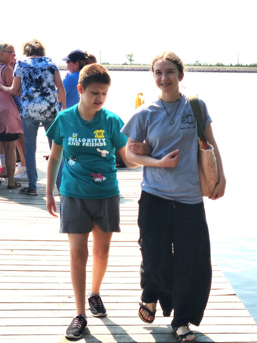 A young woman has locked arms with an instructional assistant as they walk across the dock at Mina Lake, SD