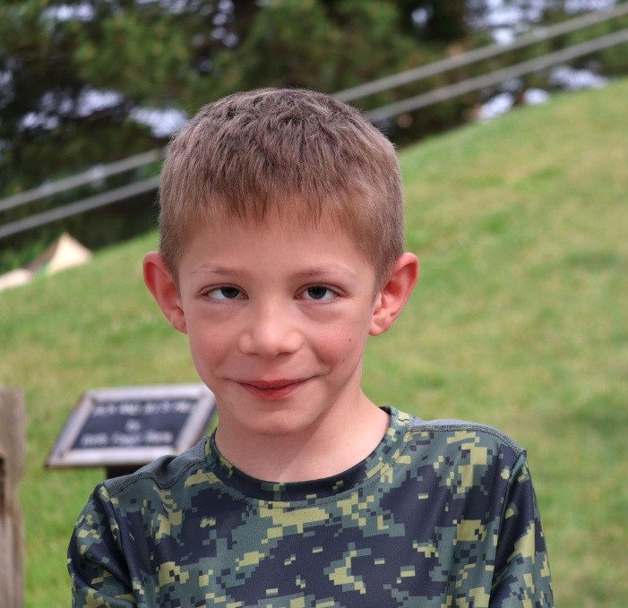 A young boy smiles at the camera with a large green hill in the background