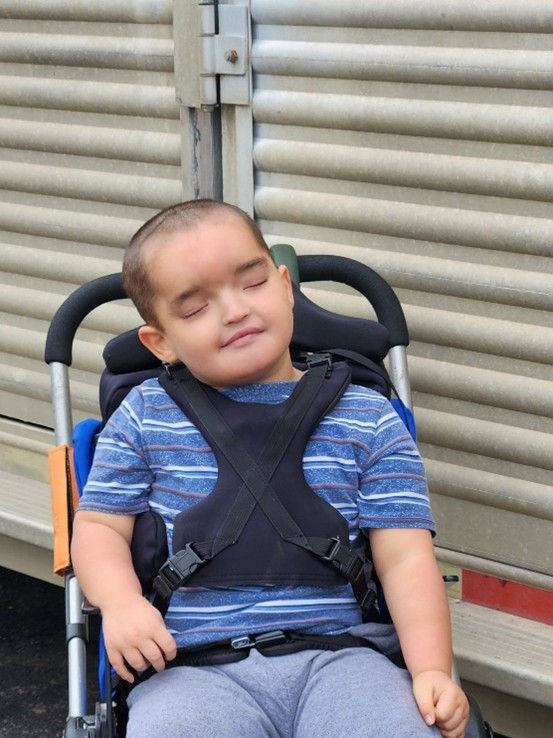 A young boy in a wheelchair sits beside a horse trailer