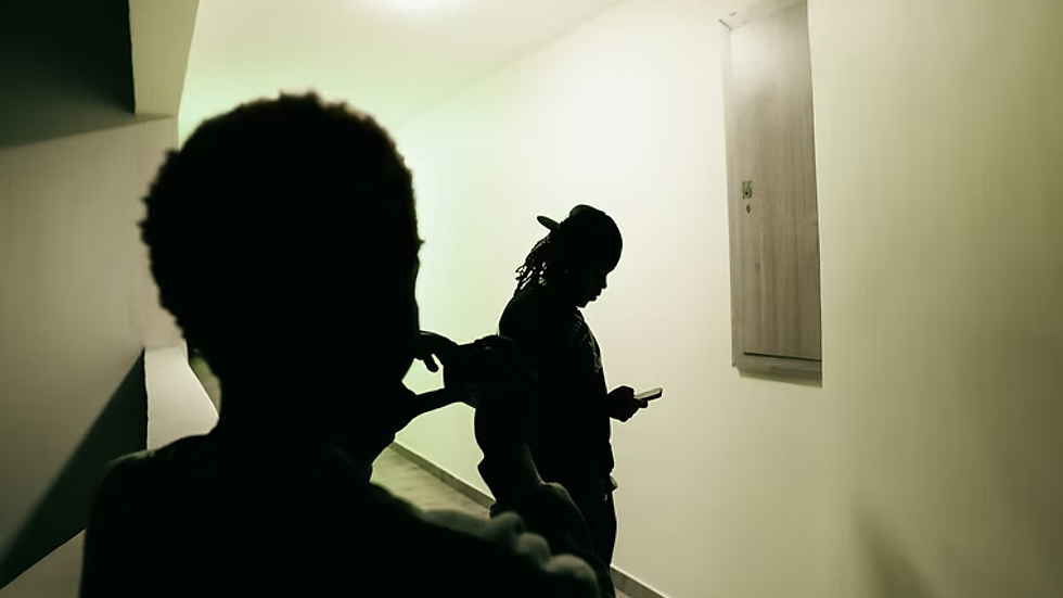 Silhouetted young people in a dim hallway, one checking a phone.