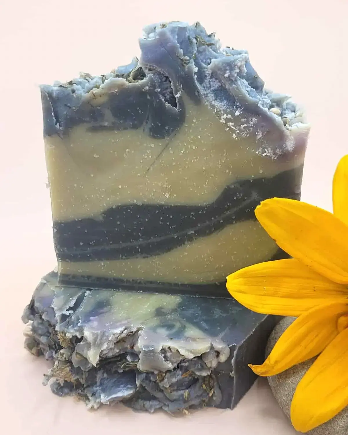 naturalne mydło konopne w kostce na jasnym tle w otoczeniu kwiatów