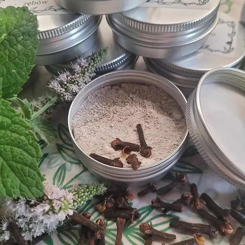 Miniatura: opakowanie goździkowego proszku do mycia zębów w otoczeniu goździków i mięty