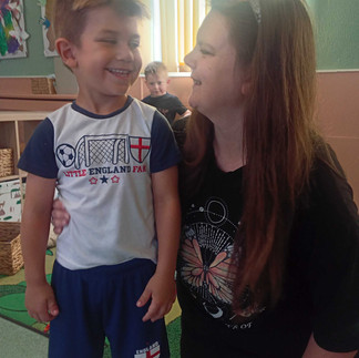 A young boy smiles at a nursery practitioner as they stand together in the playroom.