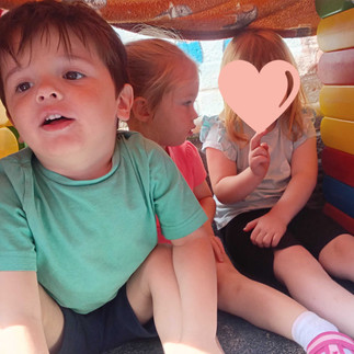 Children sitting together inside a cool garden den at Fun Box Day Nursery to escape the summer heat.