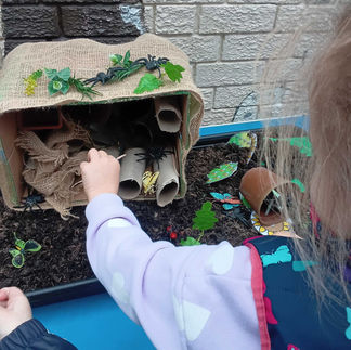 a child is playing with toy insects, placed into a bug hotel made of paper tubes, grass, leaves, soil