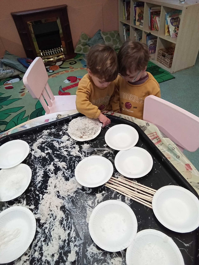 two little boys wearing the same outfit are looking at a sensory tray filled with cooked rice noodles, paper bowls and chopsticks as part of Lunar New Year Celebrations at Fun Box Day Nursery