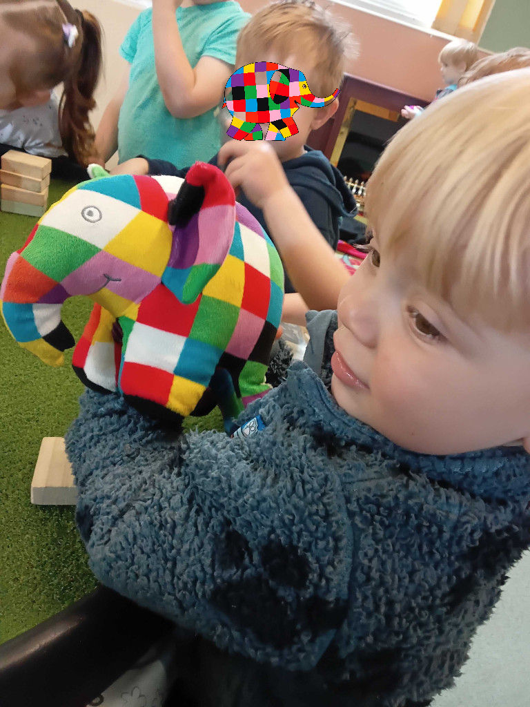 a blonde haired little boy is holding an Elmer the Elephant soft toy