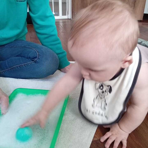a little baby is reaching toward a little ball that's in a tray full of bubbles