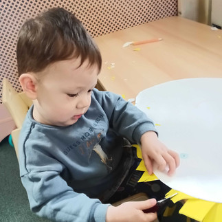 a little boy is holding a pair of scissors cutting yellow paper stripes off of a larger white circular paper