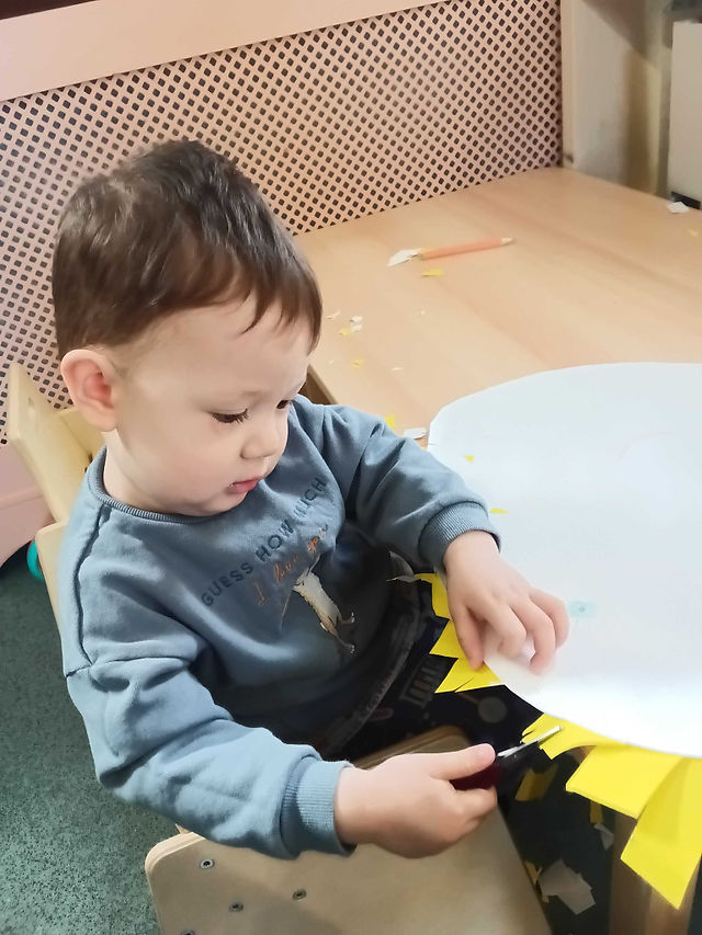 a little boy is holding a pair of scissors cutting yellow paper stripes off of a larger white circular paper