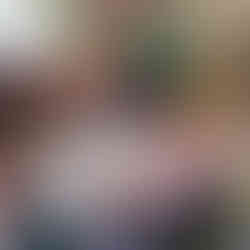 a group of children sitting around a table with white table cloth on it, a teacher wearing Fun Box Day Nursery uniform is holding up a small jar of marmalade, showing to them