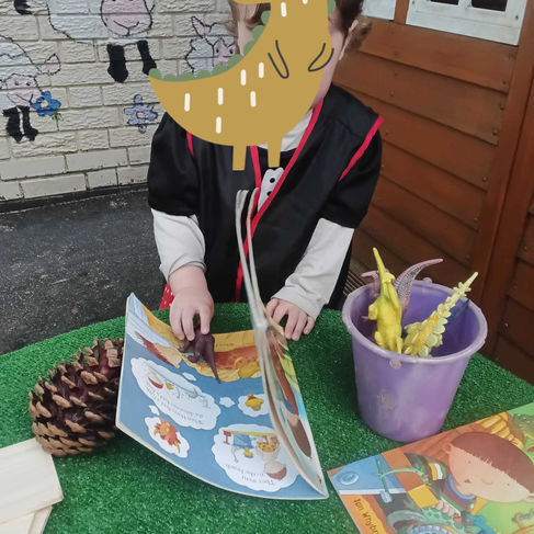 a little boy is looking at a book with dinosaurs and pinecones in front of him on a green table