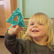 blond haired little girl is holding up a shape threading in her hand and smiling to the camera