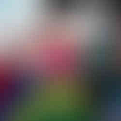 a little girl in a pink top have a massive grin while she's playing with a colourful parachute as part of a large group in the garden of Fun Box Day Nursery