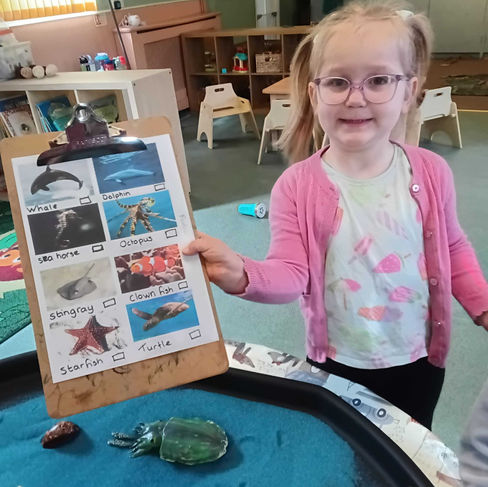 Child proudly holding a sea creature picture checklist after completing an Under the Sea treasure hunt, developing observation skills, vocabulary and confidence at Fun Box Day Nursery.