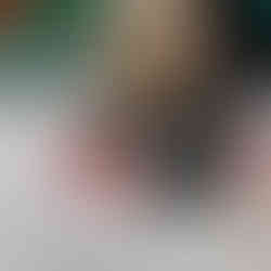 A young child with blond hair lies on their tummy on the floor, drawing on a pink house shape that is part of a large paper street activity. The child is concentrating as they add details to their picture, exploring the “Who lives in my house?” project.