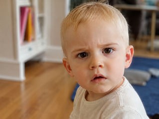 confused toddler looking directly at the camera wearing a white t-shirt
