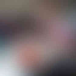 a baby girl is reaching for some colourful congs that are on a white plastic rod, she is sitting on a n adults lap, but the adult cannot be seen