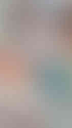 a little baby is playing with colourful stacking rings while sitting on a lightly coloured rug in a nursery baby room