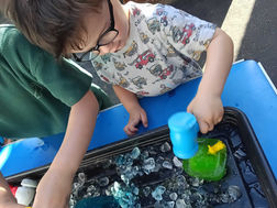 a little boy wearing glasses is trying to break a green ice block using a blue toy hammer