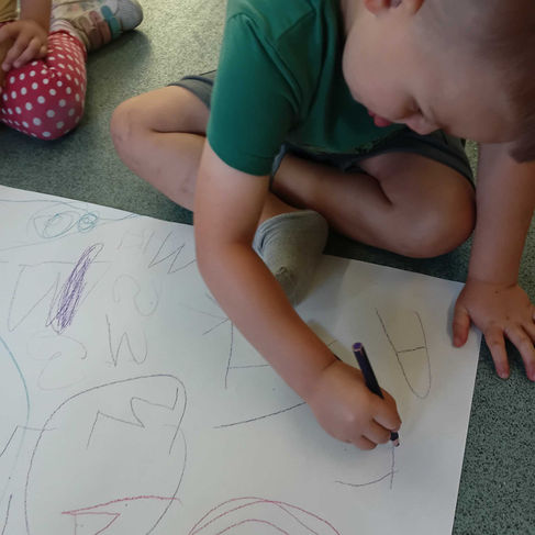 a little boy is drawing on a large paper whilst sitting on the floor, he's deep focus is shown on his face