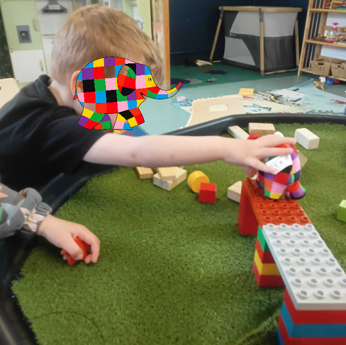a young child is playing with an Elmer soft toy on a lego bridge