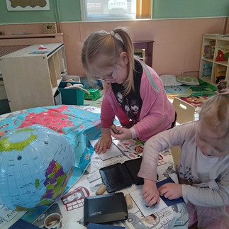 two young children are using stamps to mark the countries in their toy passport, there is a large map of the world in front of them