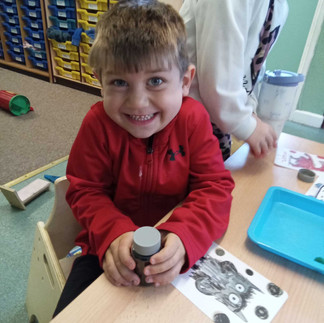 a little boy is pulling a cheeky face whilst looking into the camera, there is the black colour monster card in front of him on the table representing the emotion fear