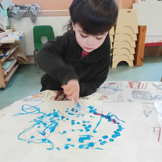 a little boy wearing black jumper is using a bingo dabber to decorate an easter egg drawn on white paper