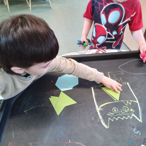 a little boy is placing a yellow triangle onto a yellow colour monster drawn on a black tray