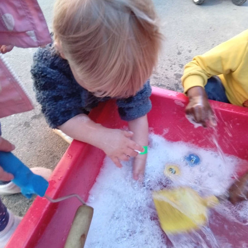 blond haired toddler is splashing soapy water in a red tray