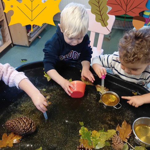 Two children concentrating at an autumn water play table, using pipettes and red bowls to explore floating leaves, pinecones and natural treasures at Fun Box Day Nursery.