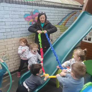 a small group of children and a teacher are pulling an expandable band over a green slide