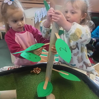 two little girls are pushing numbred green leaves into a carboard tube