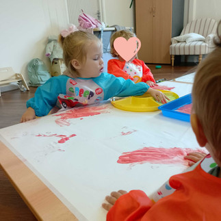 a group of young toddlers wearing aprons are making marks on a large piece of paper using edible paint made from youghurt