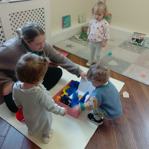 a group of young babies are exploring  a Dear Zoo themed story box with the help of their teacher